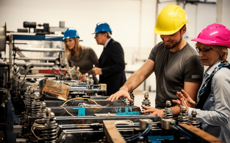 Engineers in hard hats inspecting a production machine on a factory floor