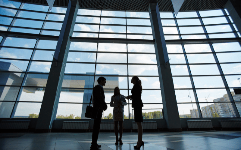 Three people in business dress talking in a glass-walled atrium