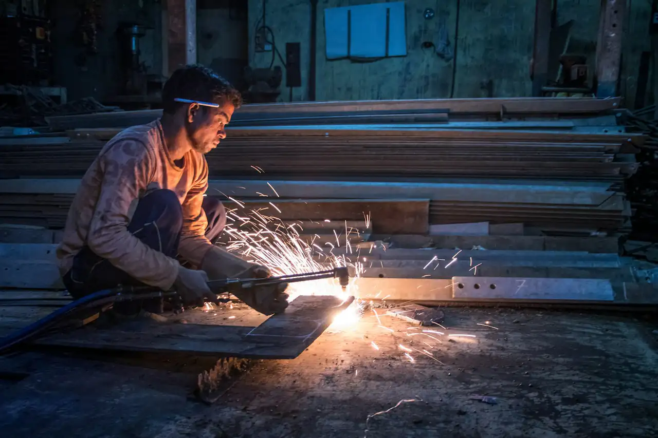 A worker cutting steel in a dim workshop, sparks flying