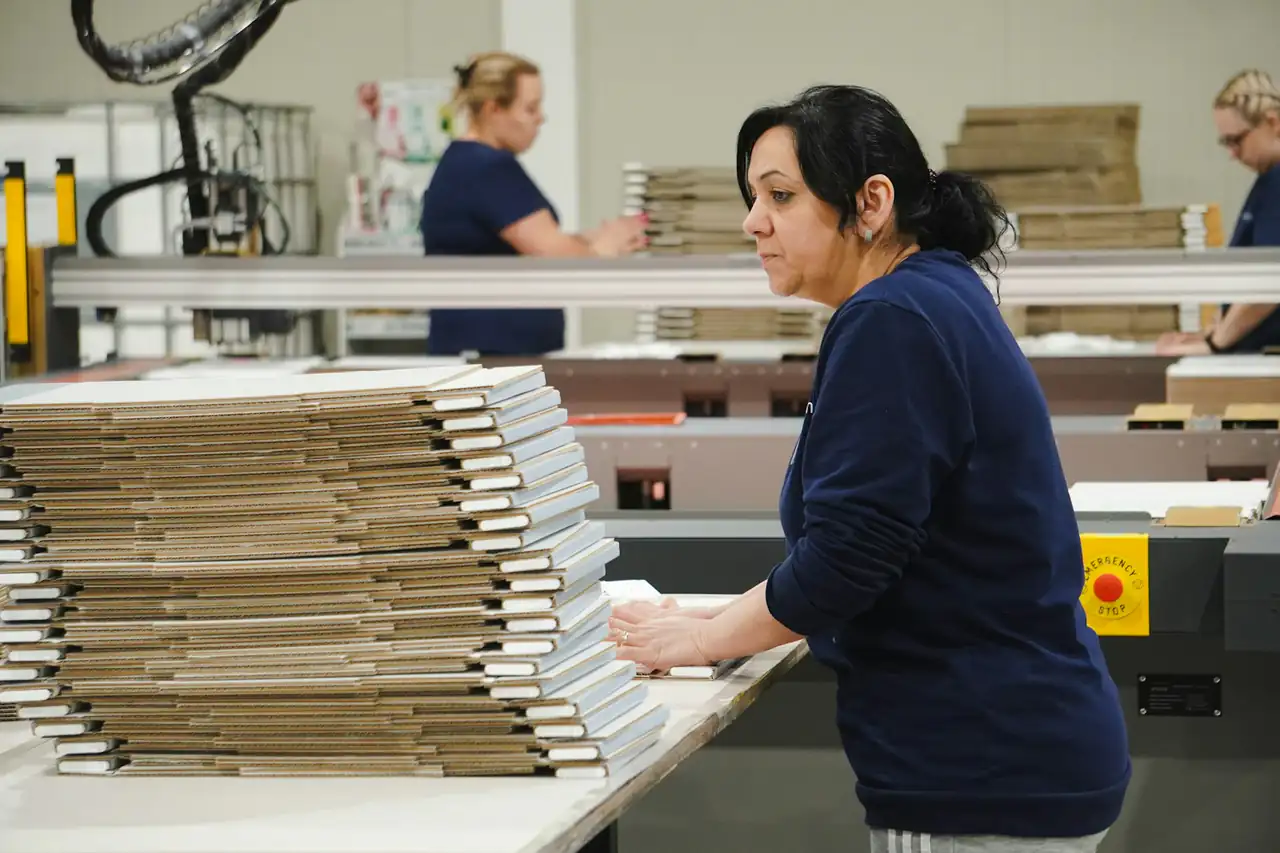 A worker stacking flat cardboard cartons in a packaging plant