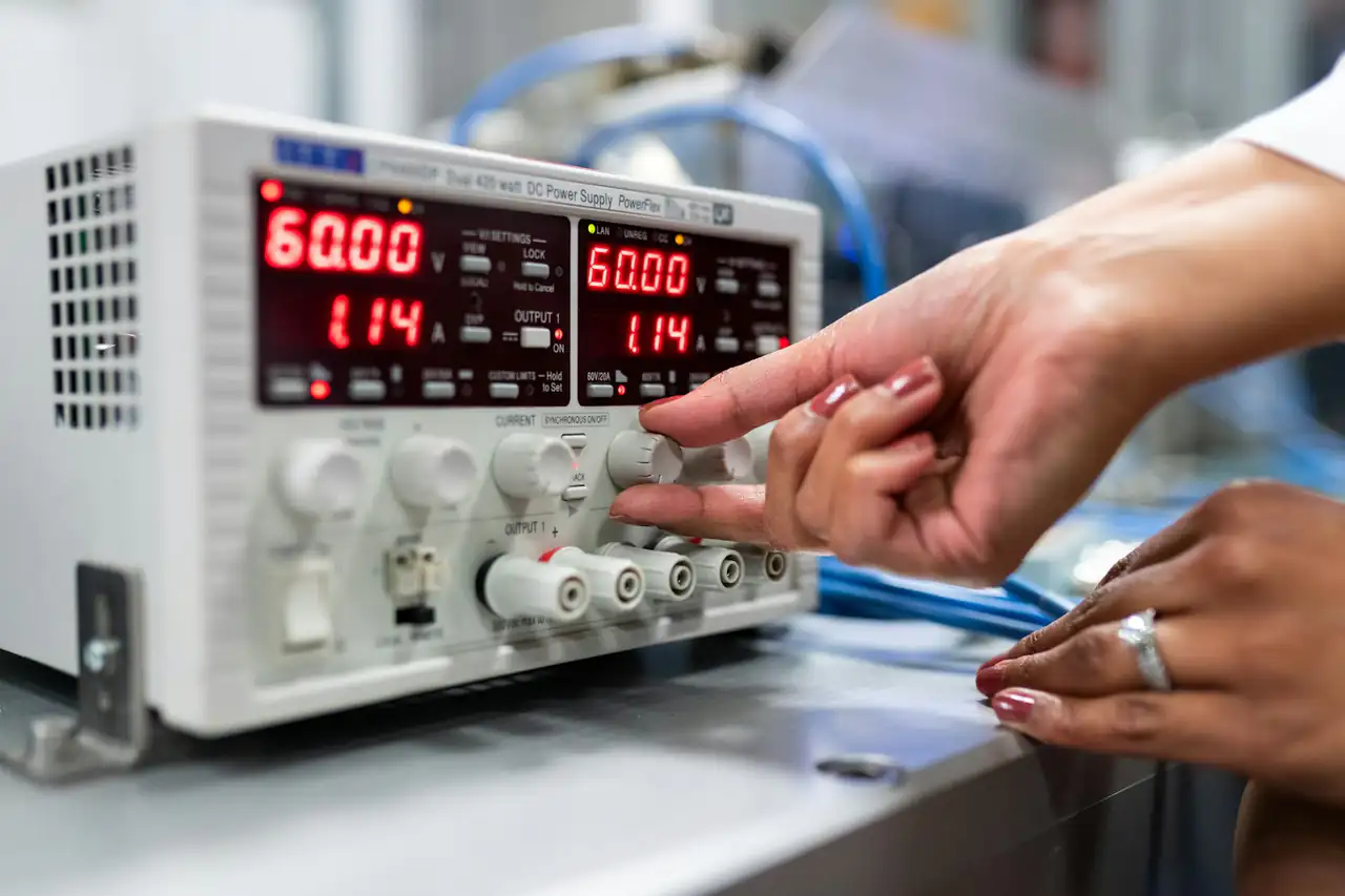 Hands adjusting a bench power supply during electrical testing