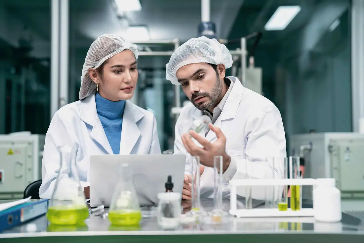 Two staff in lab coats and hairnets reviewing results in a food laboratory
