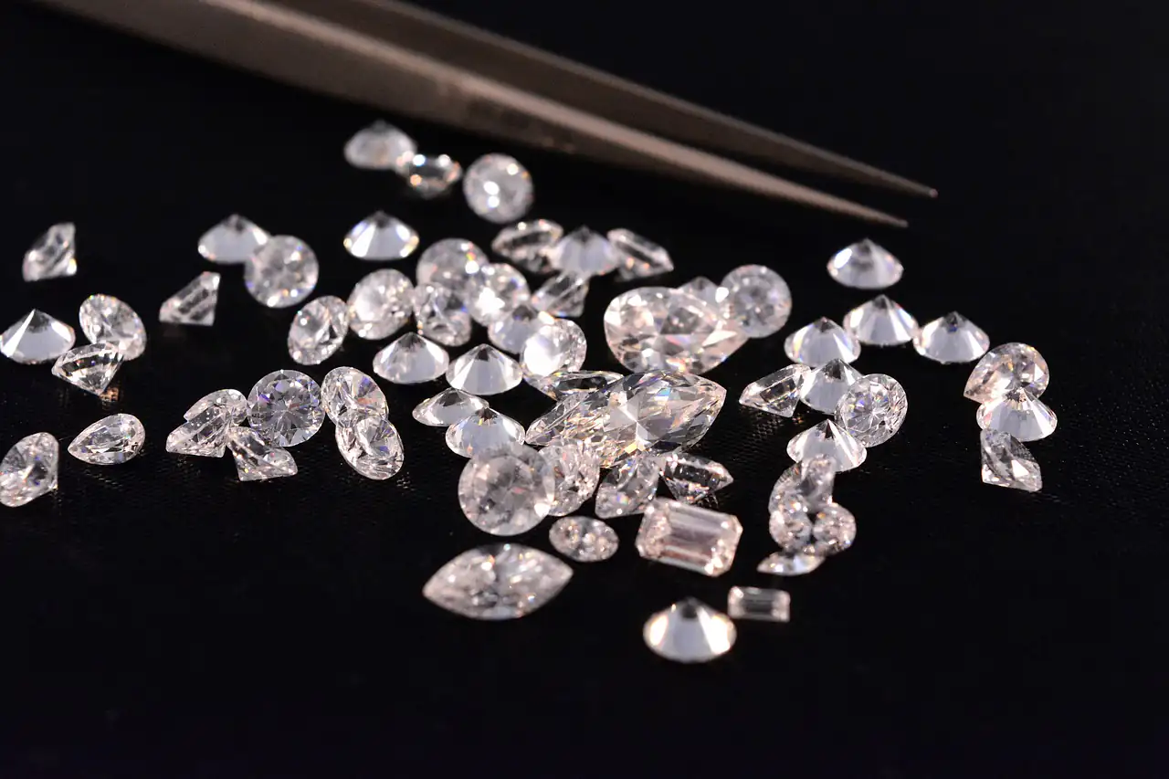 A scatter of loose cut diamonds beside a pair of tweezers