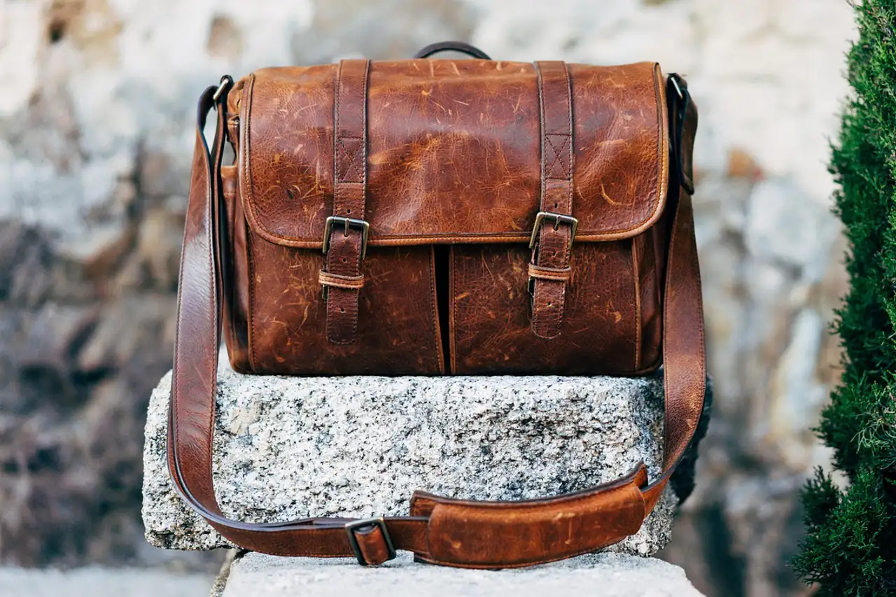 A brown leather messenger bag resting on a stone ledge