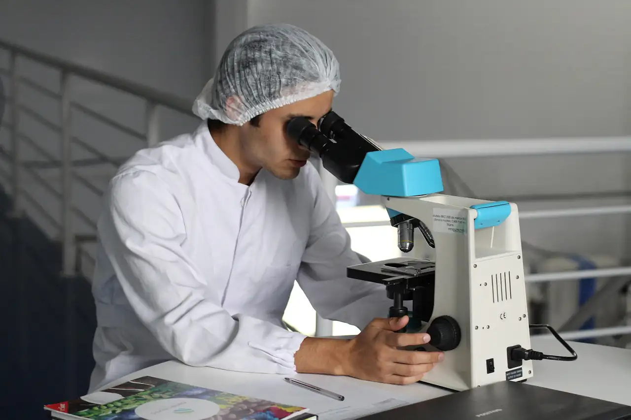 A lab worker in a hairnet looking through a microscope