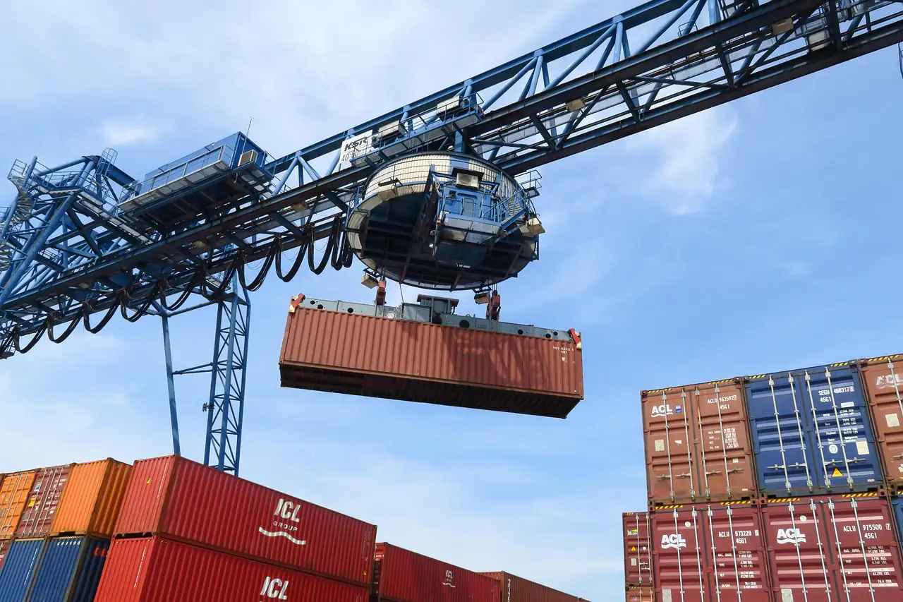 A crane spreader lifting a container above stacked boxes