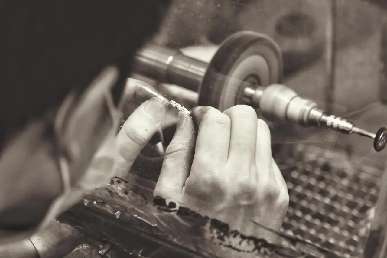 A metalworker polishing a piece at the wheel