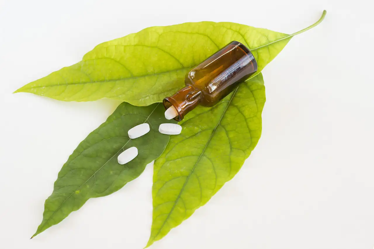 A small dropper bottle and tablets on a green leaf