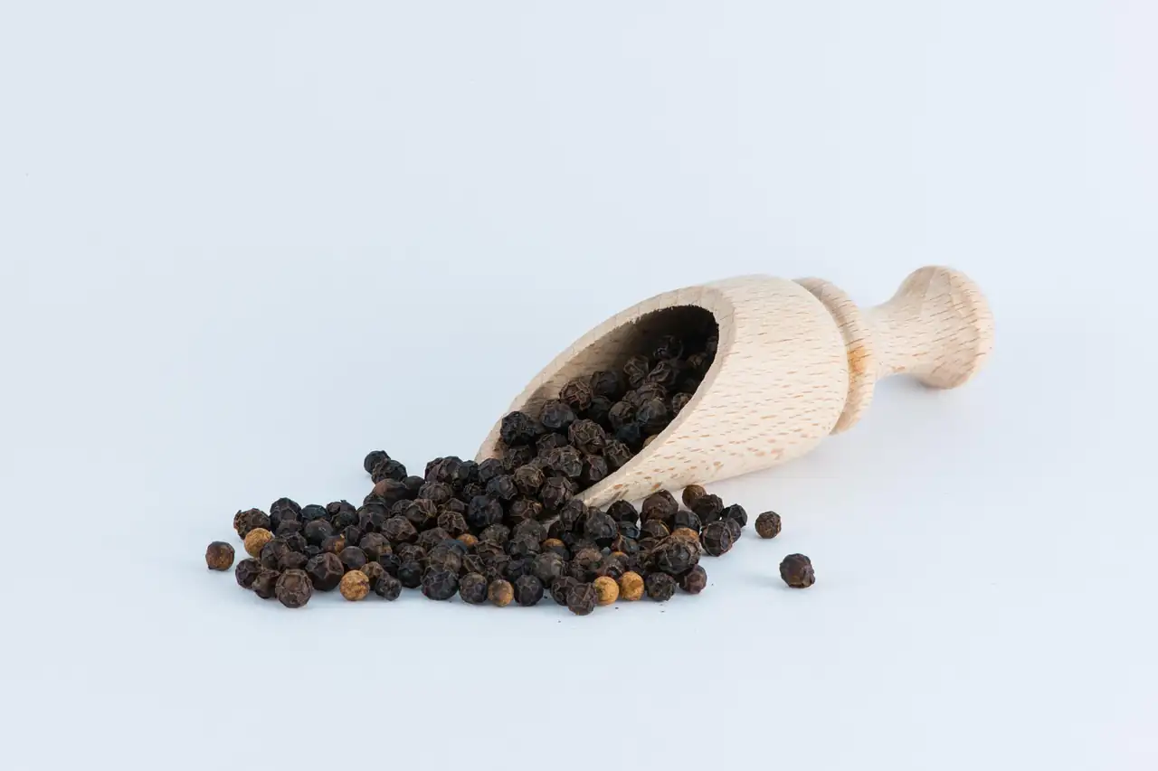 A wooden scoop of black peppercorns