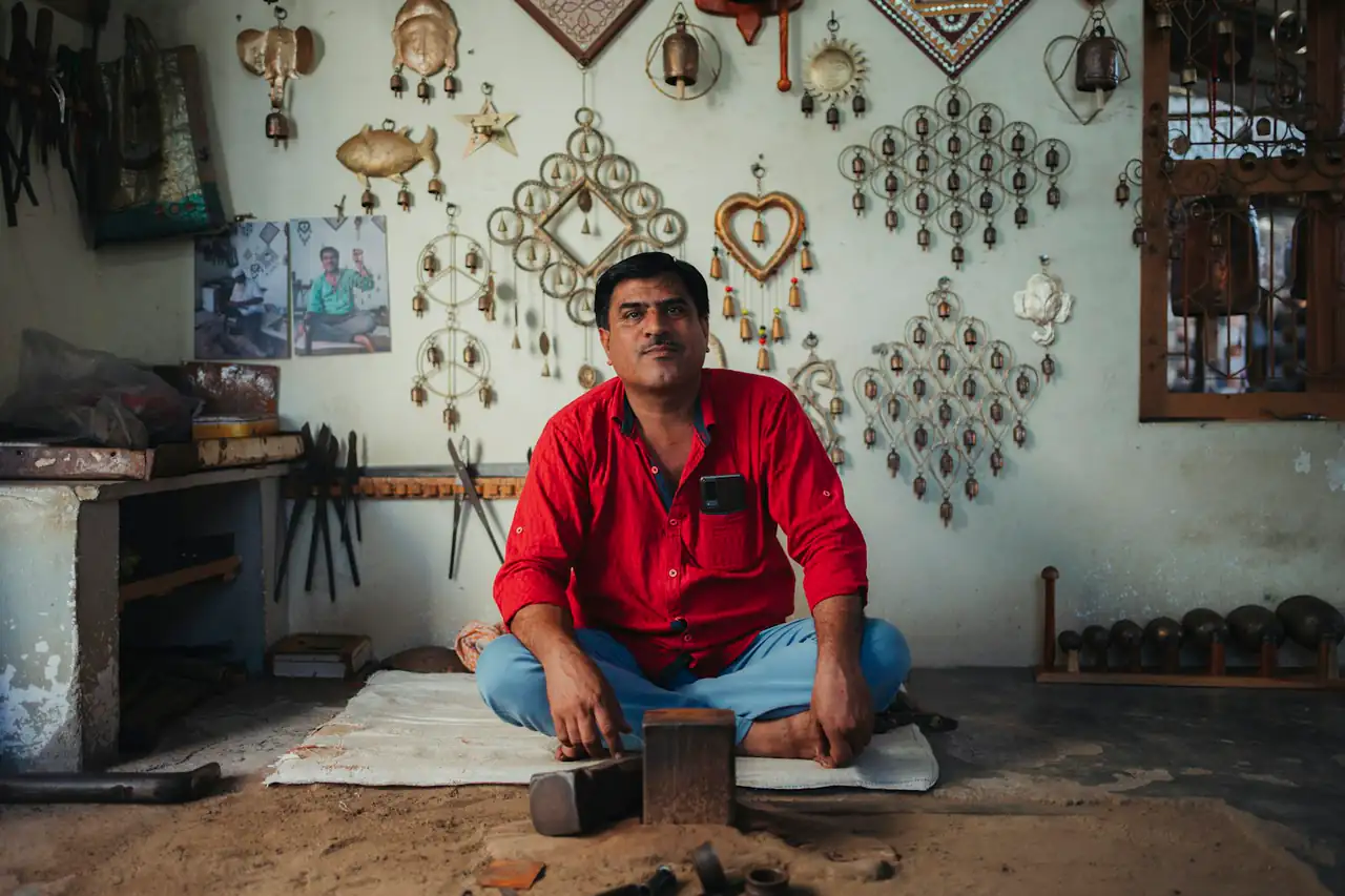 A craftsman seated in his workshop surrounded by finished metal pieces