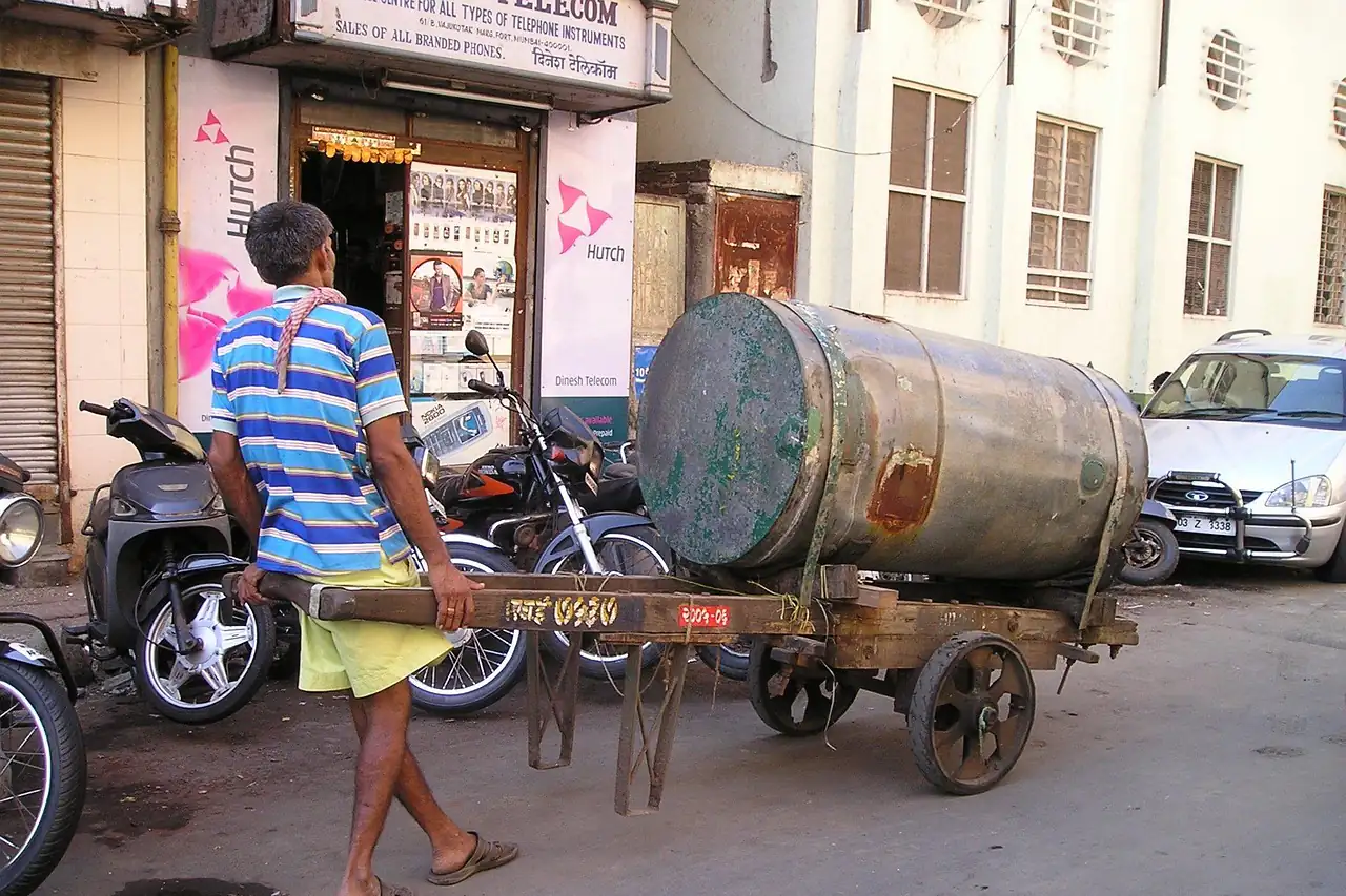 A man hauling a tank on a cart through a town street