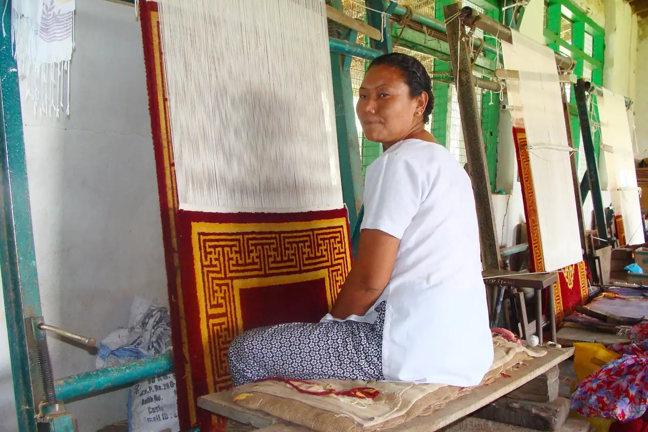 A weaver seated at an upright carpet loom