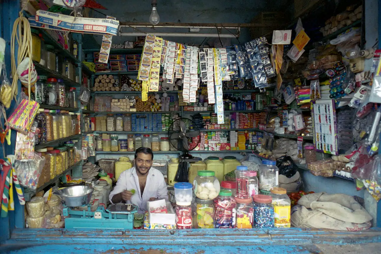 A shopkeeper behind a counter packed with goods
