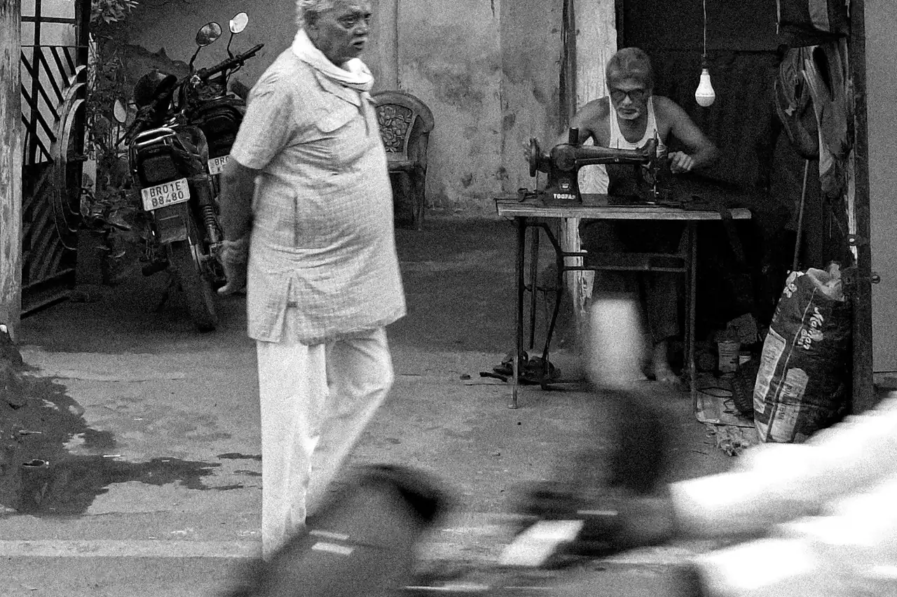 An older man standing outside a small tailoring workshop