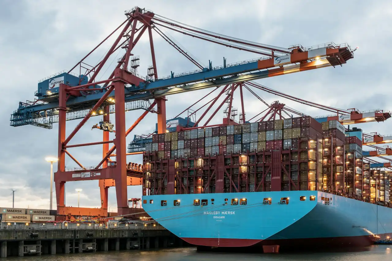 A container ship being worked under quay cranes