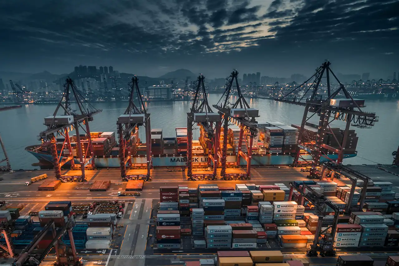 Container cranes and stacked boxes at a port terminal at dusk