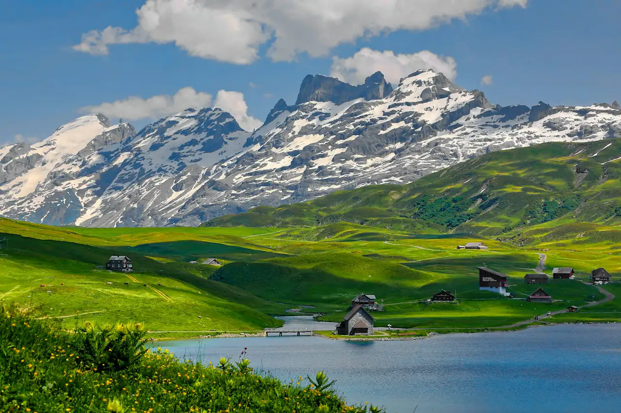Snow-capped mountains above a green valley and lake