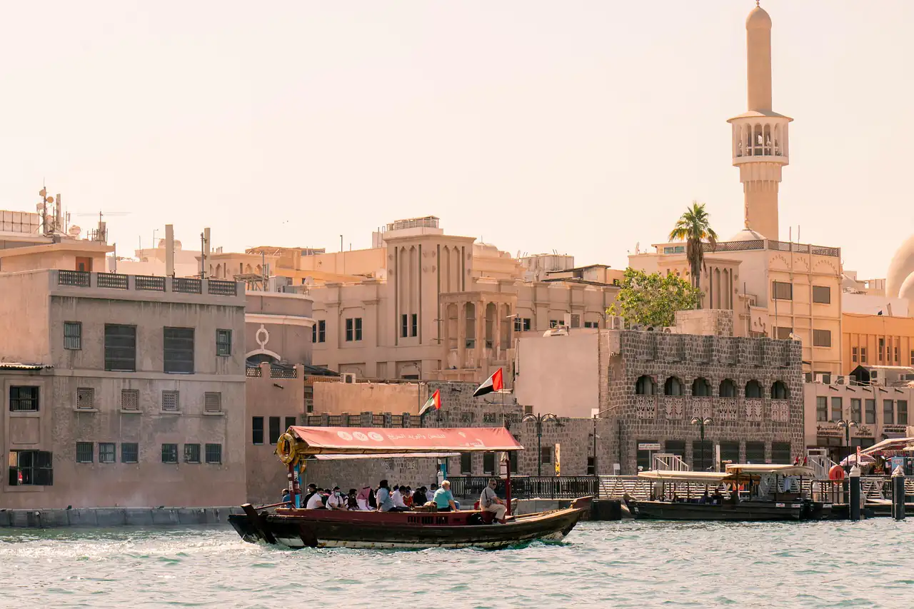 A wooden boat crossing a creek past old buildings
