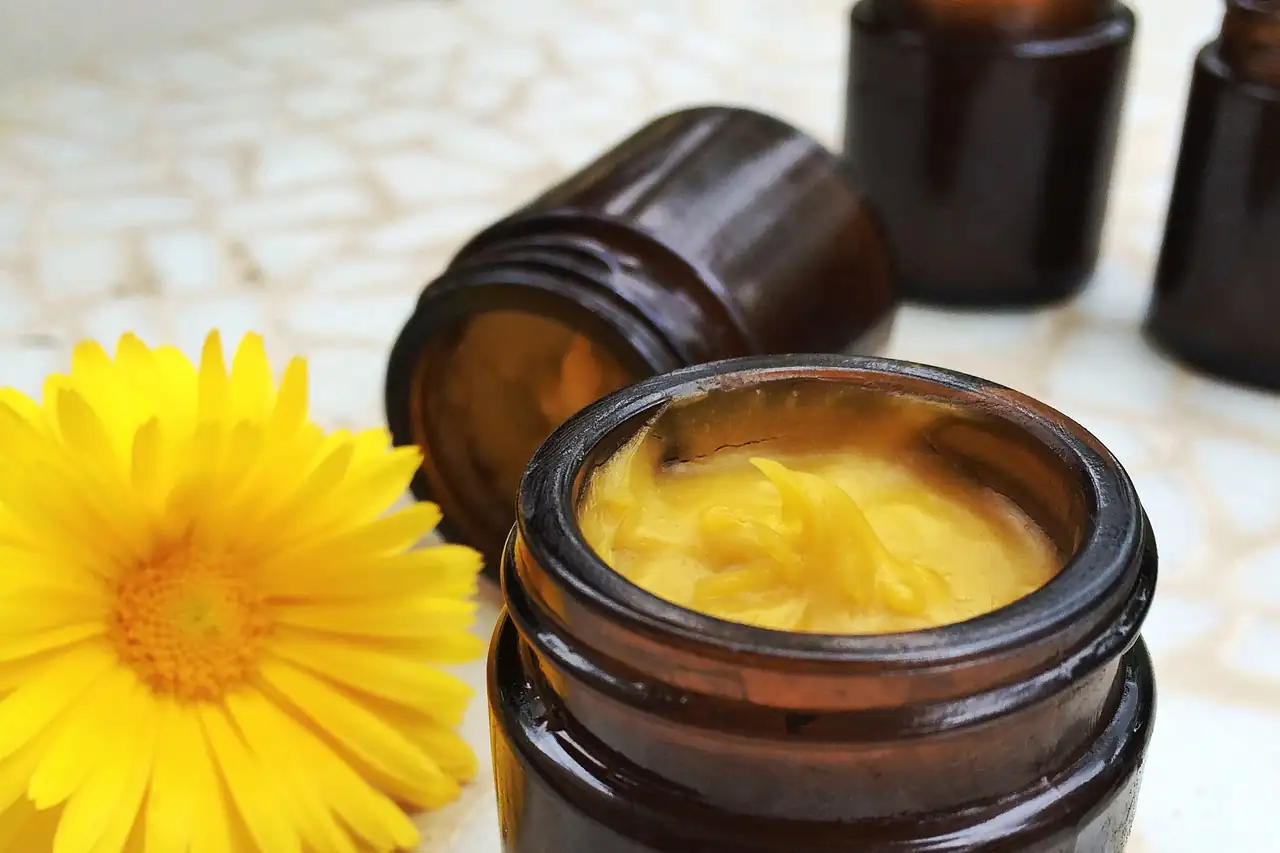 A jar of herbal cream beside a marigold