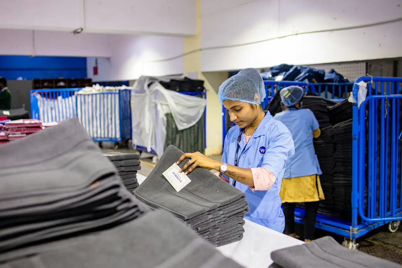 A worker inspecting grey fabric pieces on a garment factory table