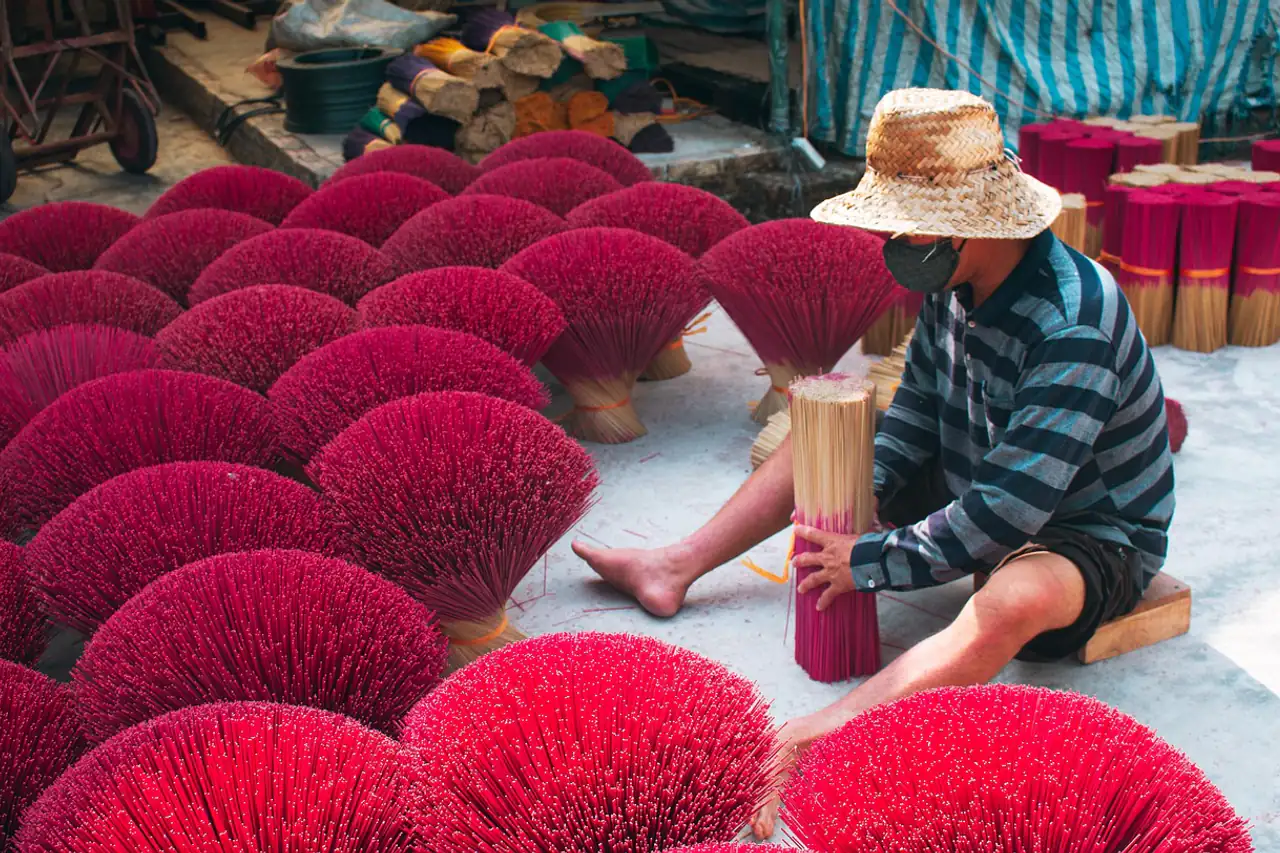 A worker sorting bundles of red incense sticks laid out to dry