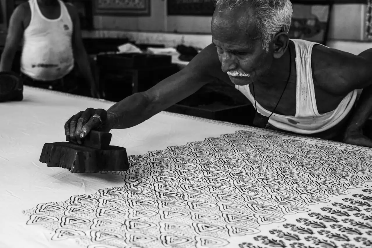 A craftsman pressing a carved wooden block onto cloth to print a pattern