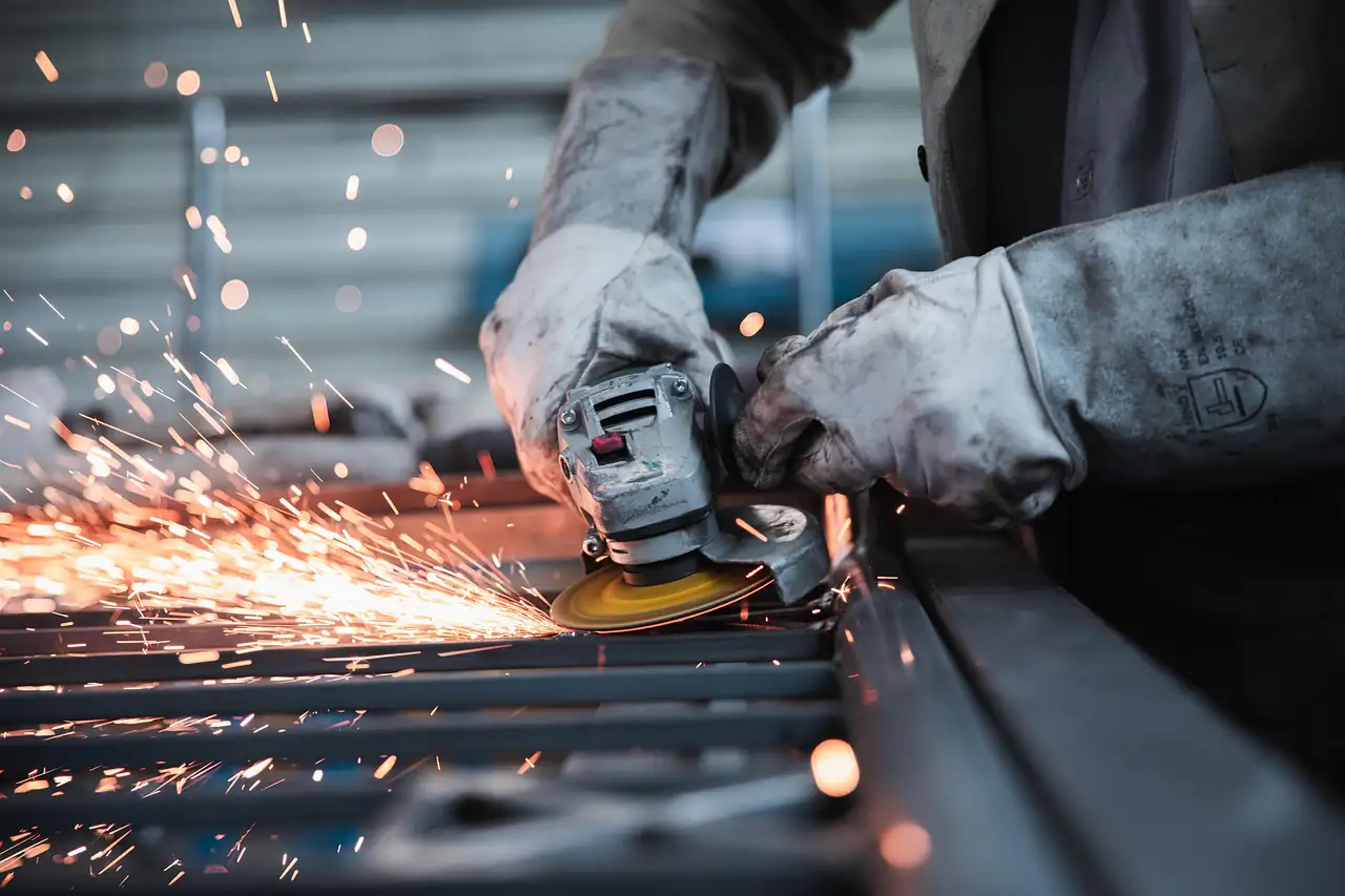 Sparks flying from a grinder as a gloved worker cuts metal